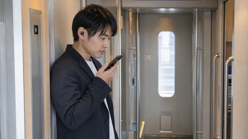 新幹線のデッキでスマートフォンを口元に近づけ小声で通話する男性