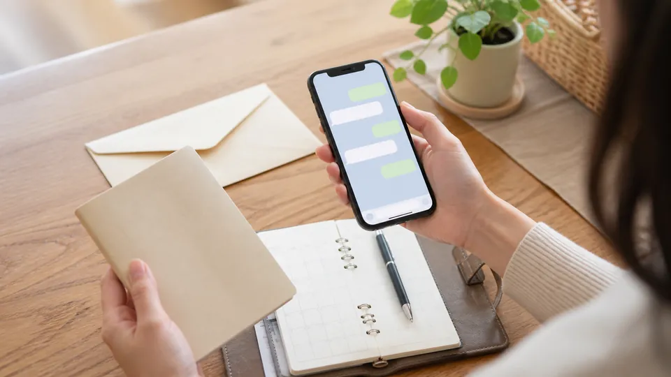 スマートフォンと手帳を前に連絡方法を考える人