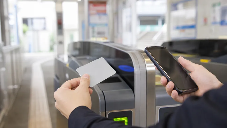 駅の改札で交通系ICカードとスマートフォンを持つ手元